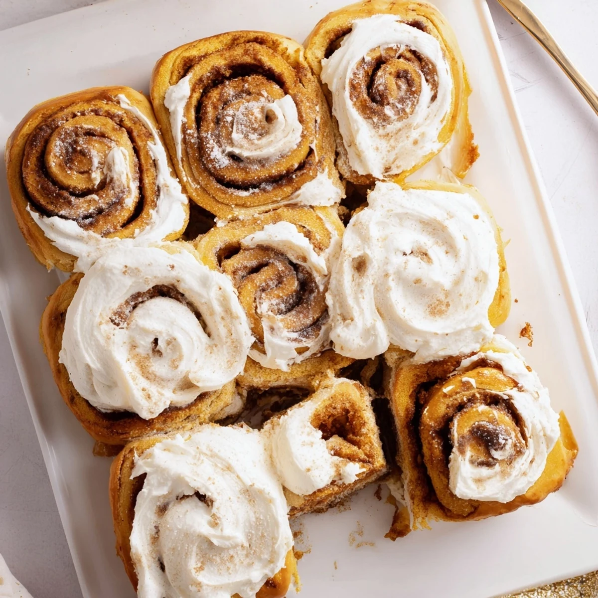Freshly baked pumpkin cinnamon rolls with cream cheese frosting on a rustic wooden table, served warm.  