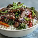 A steaming bowl of easy homemade teriyaki beef served over fluffy rice with sautéed broccoli and peppers.