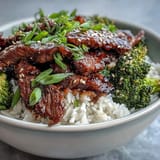 Steamed broccoli crowns a sizzling Beef and Broccoli Bowl garnished with scallions and sesame seeds. 