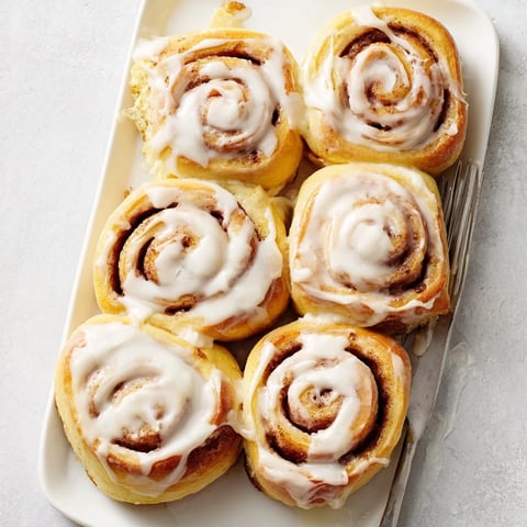 Golden-brown Pillow Soft Cinnamon Rolls topped with creamy glaze in a baking dish, ready to serve for breakfast.