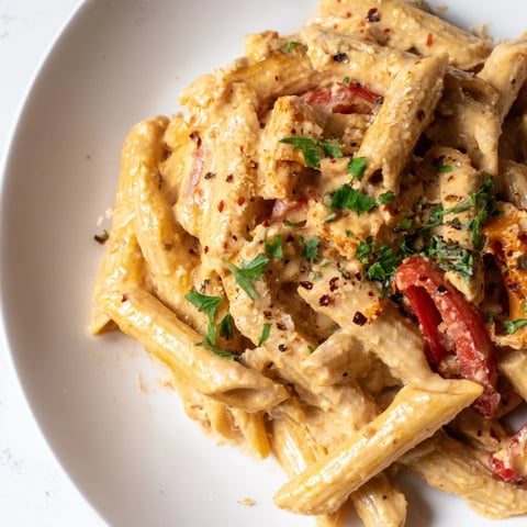 Creamy Cajun pasta in a white bowl with roasted red bell peppers, a fork ready to twirl the saucy penne.