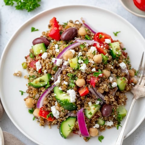 A close-up of the Greek Power Salad, with vibrant cherry tomatoes, diced cucumber, and crumbled feta over quinoa and lentils.  