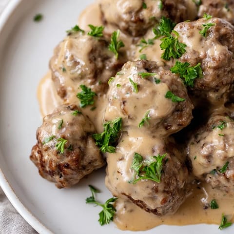 A close-up of perfectly browned Swedish Meatballs, ready to be served over mashed potatoes.