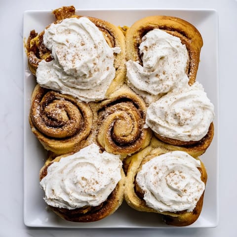 Spiraled pumpkin cinnamon rolls topped with thick cream cheese glaze, arranged on a cozy autumn breakfast plate.  