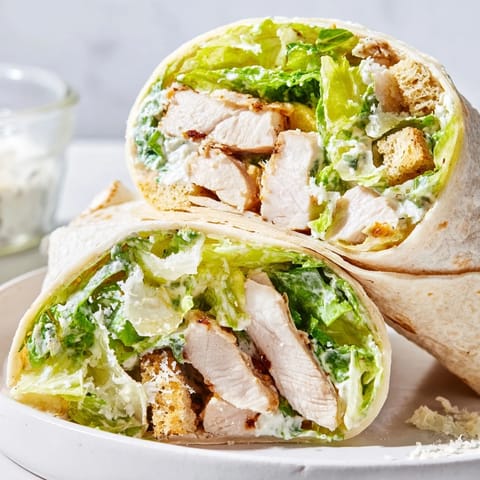 Juicy grilled chicken slices and crunchy romaine leaves bundled in a warm tortilla, showcasing a Caesar Chicken Salad Wrap with parmesan shavings and croutons.  
