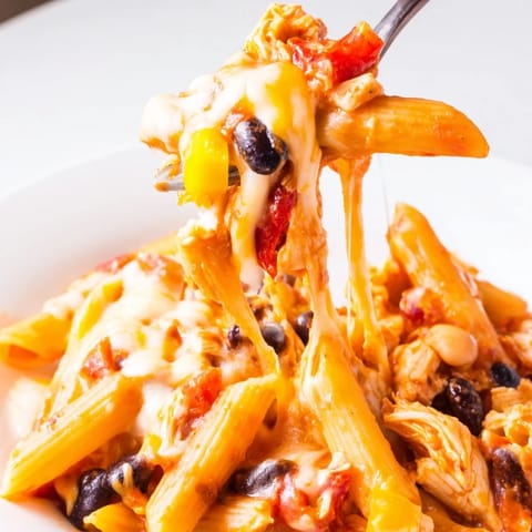 A close-up of Chicken Enchilada Pasta featuring penne noodles, black beans, and chicken in a rich red enchilada sauce.