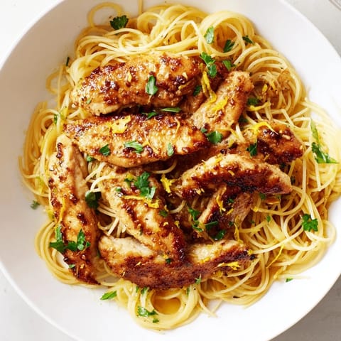 A close-up of Brown Butter Lemon Chicken Pasta glistening with a glossy sauce and lemon wedges on the side.  