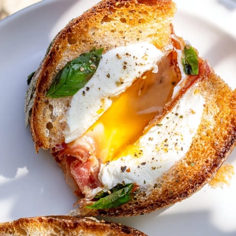 Slices of golden, buttery sourdough reveal melted burrata and crispy prosciutto in this Crispy Prosciutto & Burrata Grilled Cheese, served warm on a wooden board.