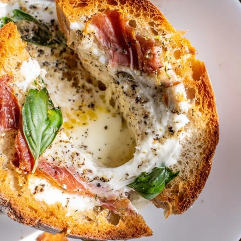 This Crispy Prosciutto & Burrata Grilled Cheese shows melted burrata peeking out from crisp prosciutto between golden, buttery sourdough, perfect with fresh basil and a glass of white wine.