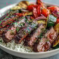 Juicy grilled steak slices and vibrant roasted vegetables sit atop fluffy rice in a finished Sheet Pan Steak and Veggie Bowl.