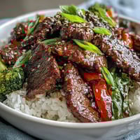 Glazed teriyaki beef bowl with crisp vegetables and fluffy rice, topped with sesame seeds and green onions.